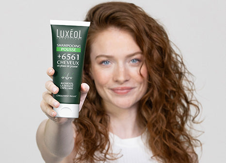 Woman holding a Luxeol shampoo bottle with a plain background