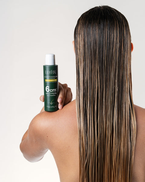 Person holding a bottle of Luxeol hair product with long, straight hair.