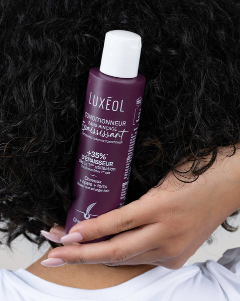 Person holding a Luxéol hair care product bottle against dark hair