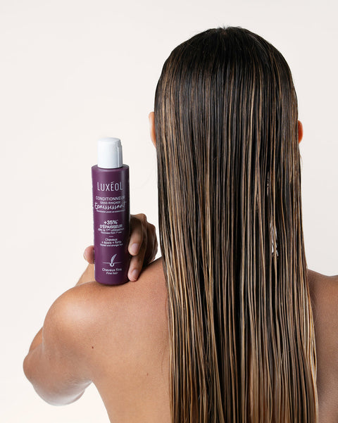 Person holding a bottle of Luxe Oil hair product with long, straight hair.
