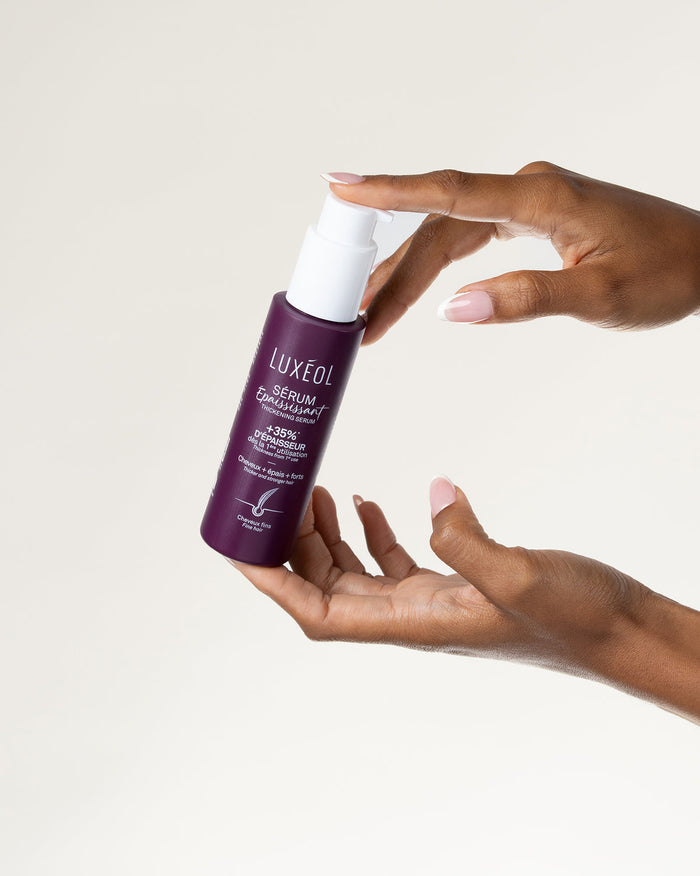 Hand holding a Luxéol hair serum bottle against a plain background